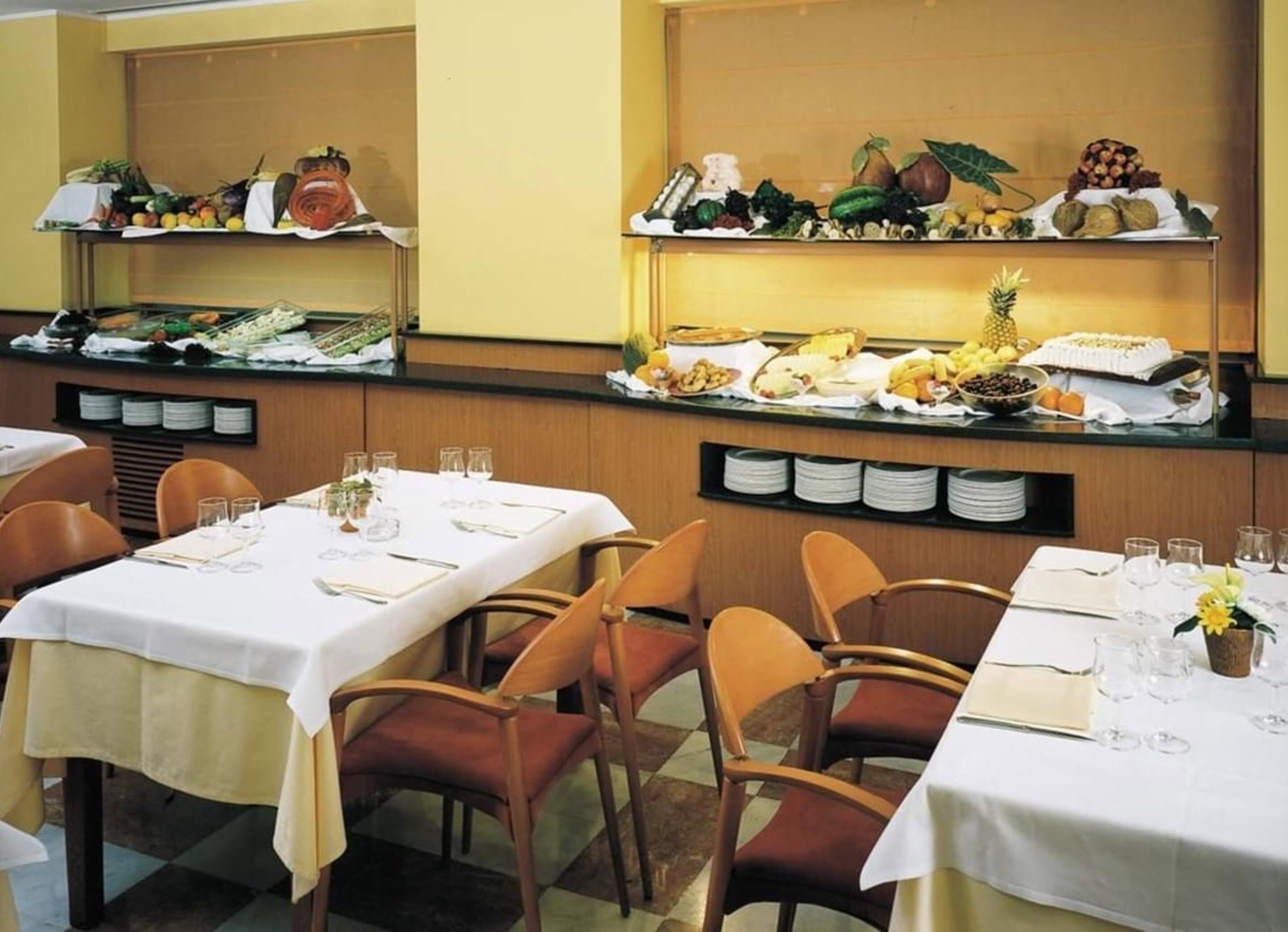 Montaje de bufé con diversos alimentos, platos y vasos sobre mesas.