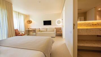 A modern hotel room with a large bed, a sofa, a desk, and a bathroom with a vanity.