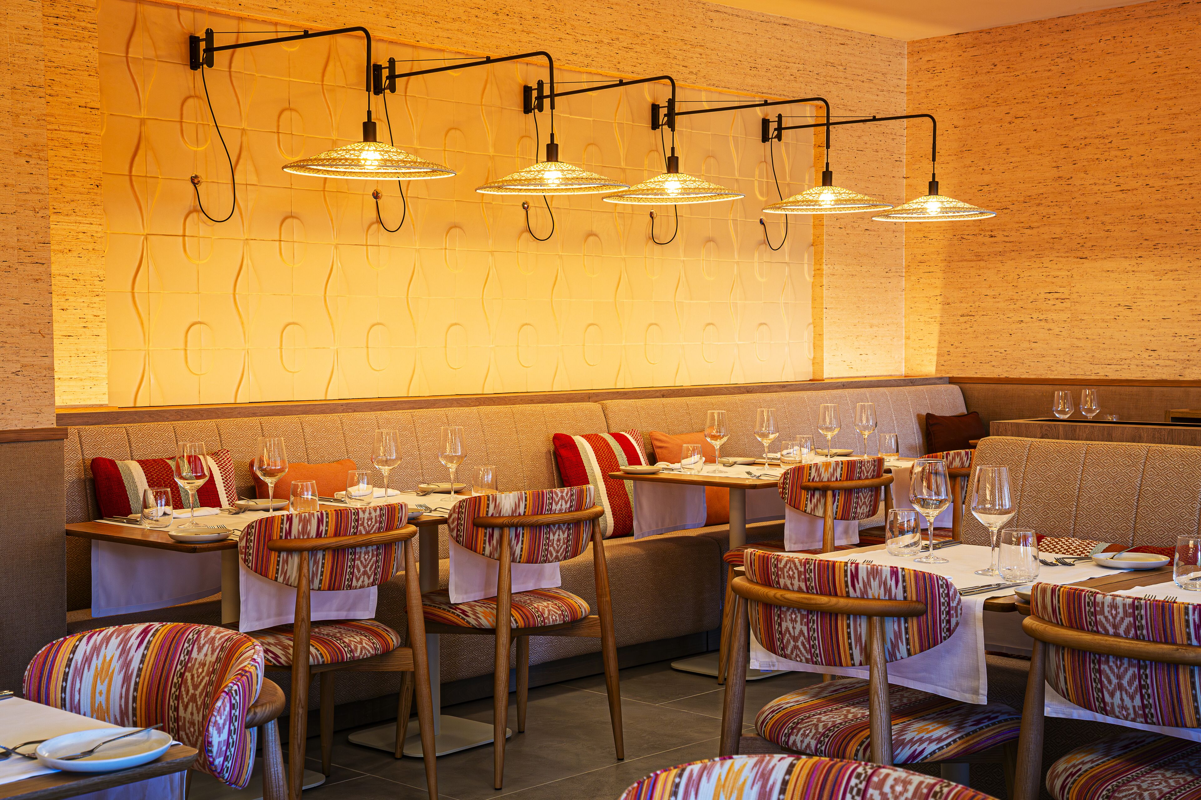 Et restaurantinteriør med flere borde og stole, hvert dækket med vinglas og bestik.