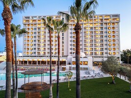 Un hotel con varios pisos, piscina y palmeras.