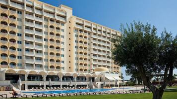 A multi-story hotel with balconies, a swimming pool, and a well-maintained lawn.