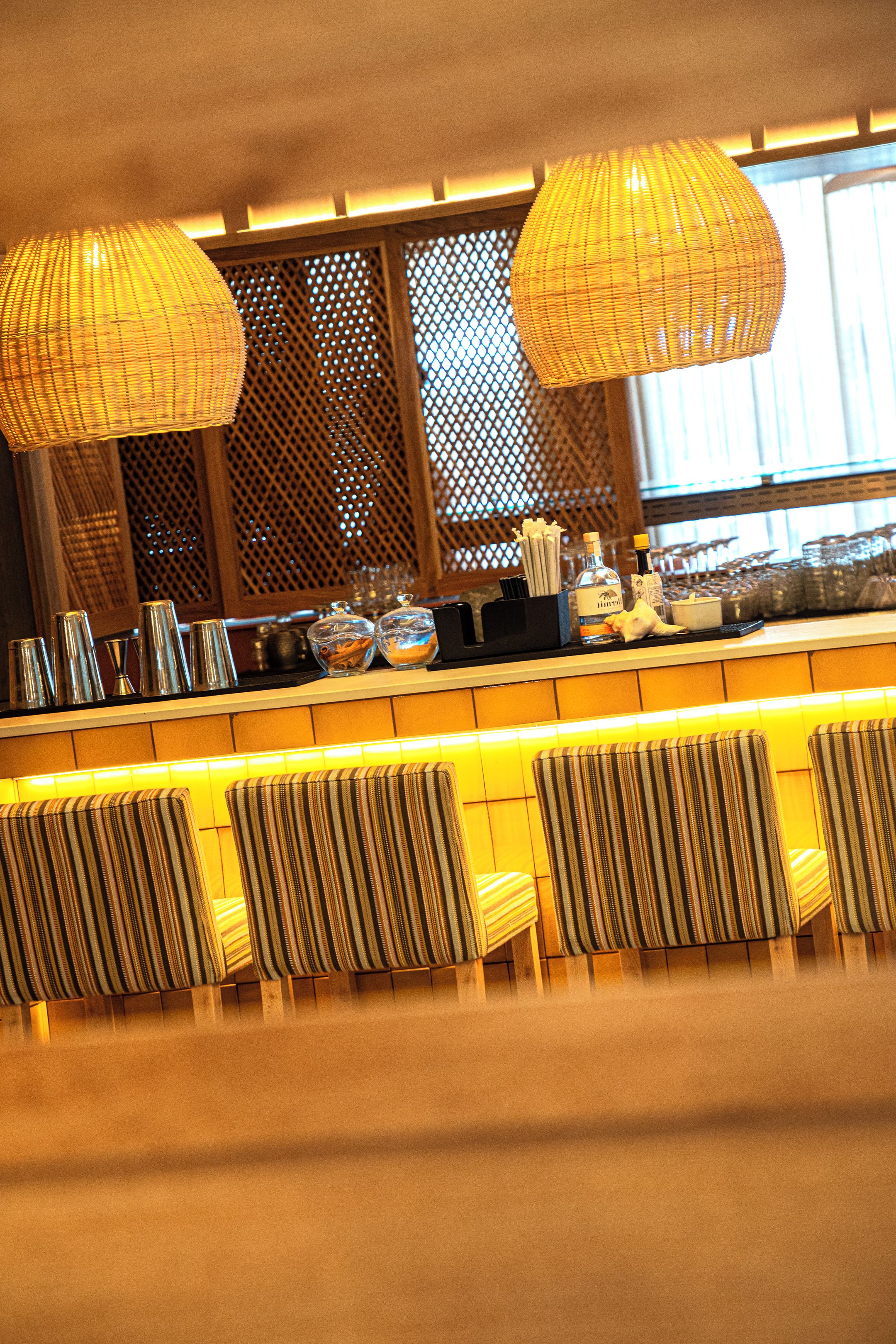 Eine Bar mit Korbstühlenlampen, einer Theke mit Flaschen, Gläsern und einer Speisekarte.
