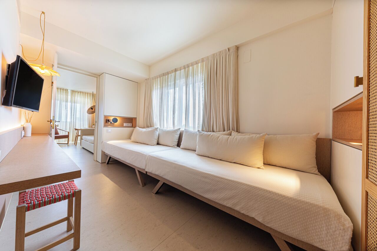 A modern hotel room with a long sofa, a television, a desk, and a chair.