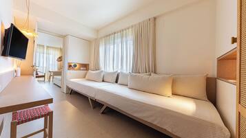A modern hotel room with a long sofa, a television, a desk, and a chair.
