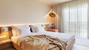 Ein modernes Hotelzimmer mit einem großen Bett, Nachttischlampen, einem Nachttisch, einem kleinen Beistelltisch, einem Fenster mit durchsichtigen Vorhängen und Blick auf Gebäude außerhalb.
