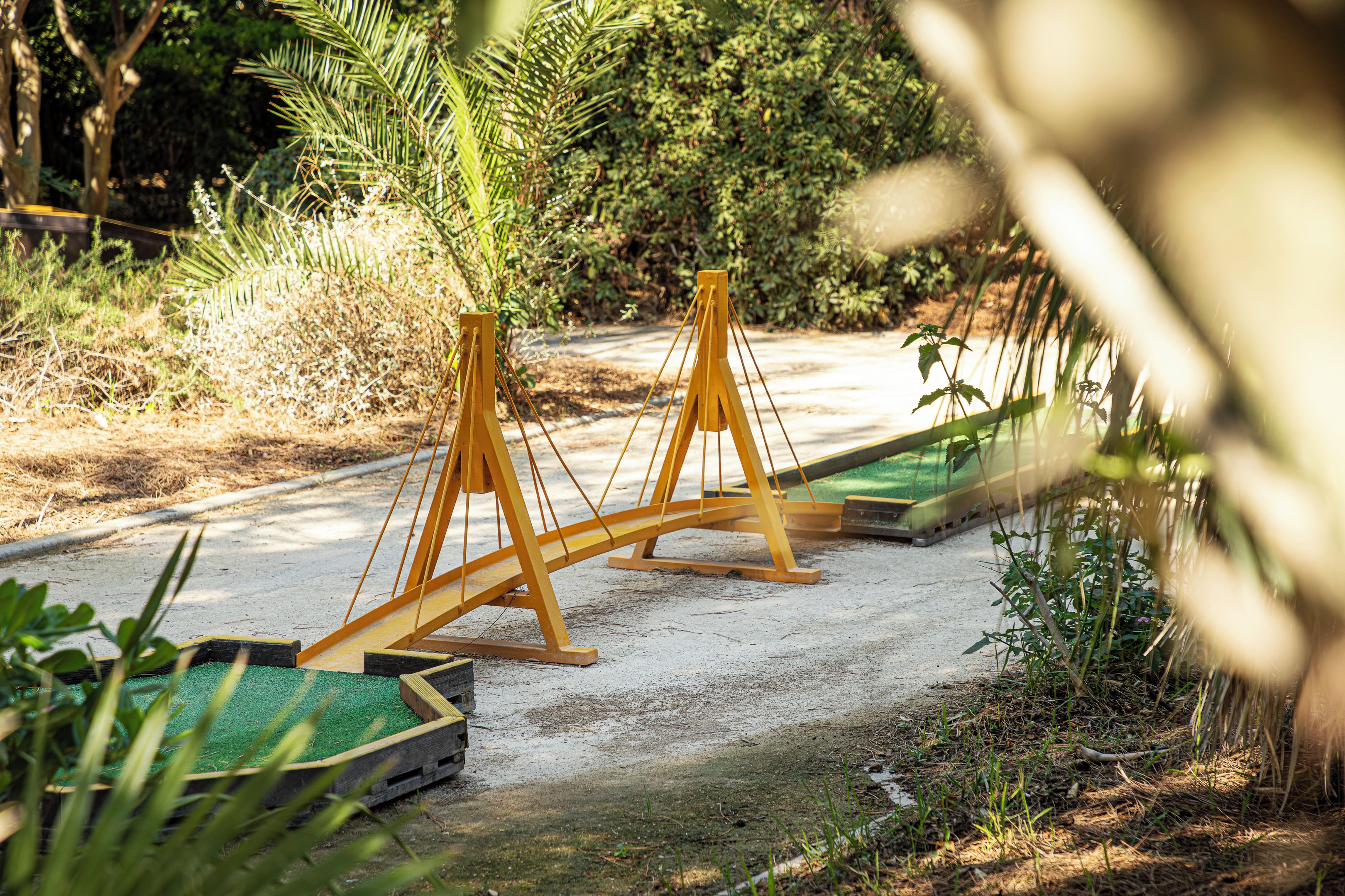 A pathway with two wooden swing sets and green planters along the sides.