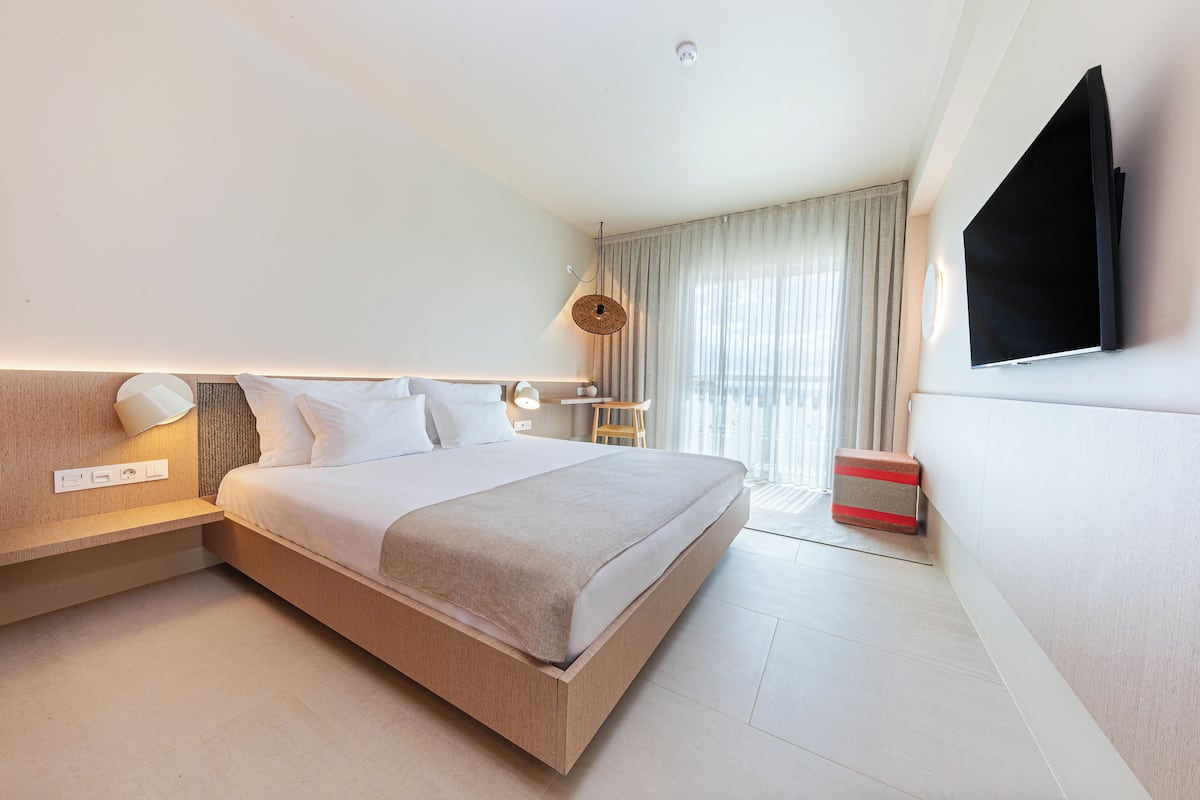 A modern hotel room with a large bed, bedside tables, a flat-screen TV, and a window with curtains.