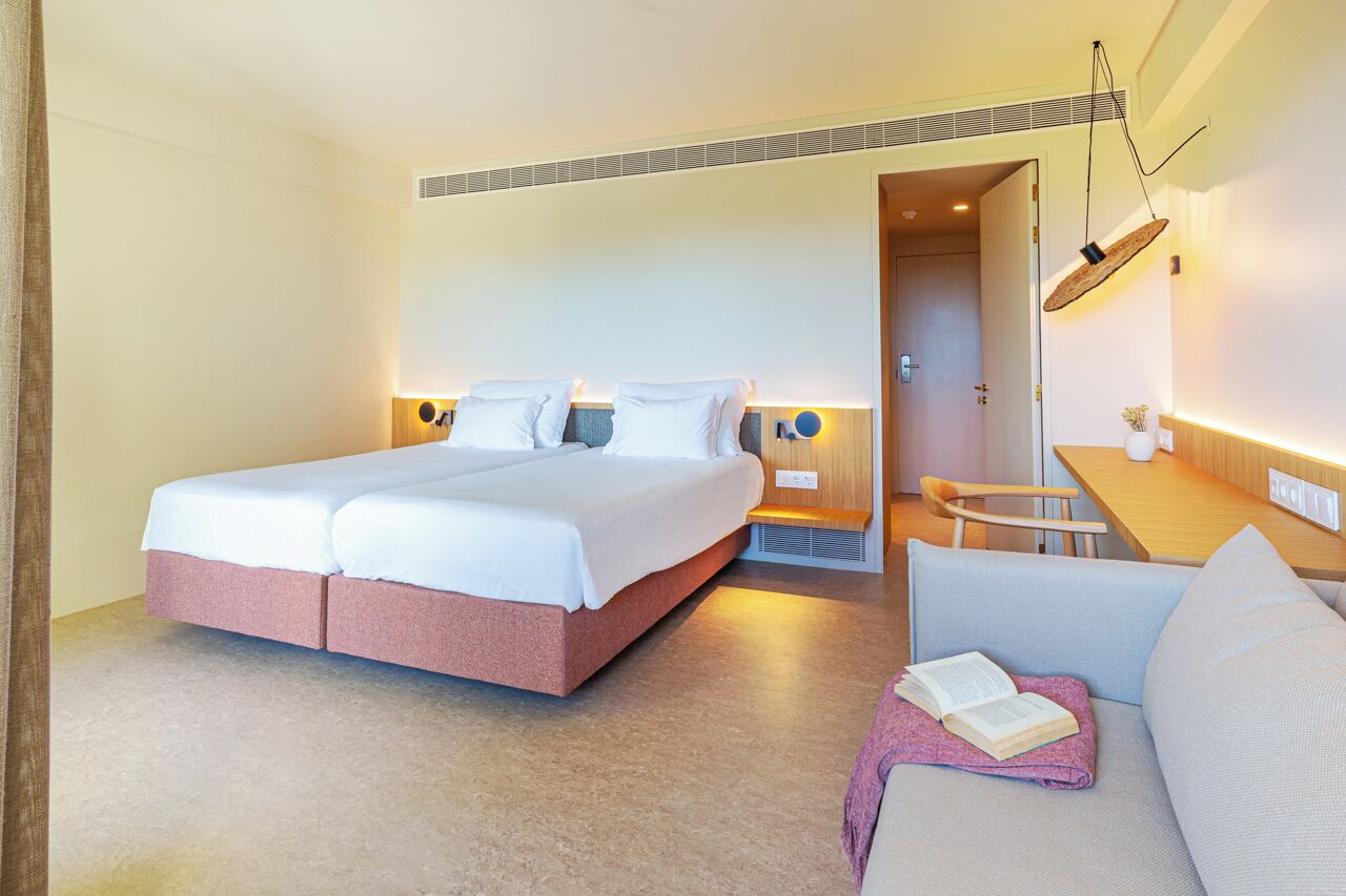 A hotel room with a double bed, a sofa, a small table, and a desk.