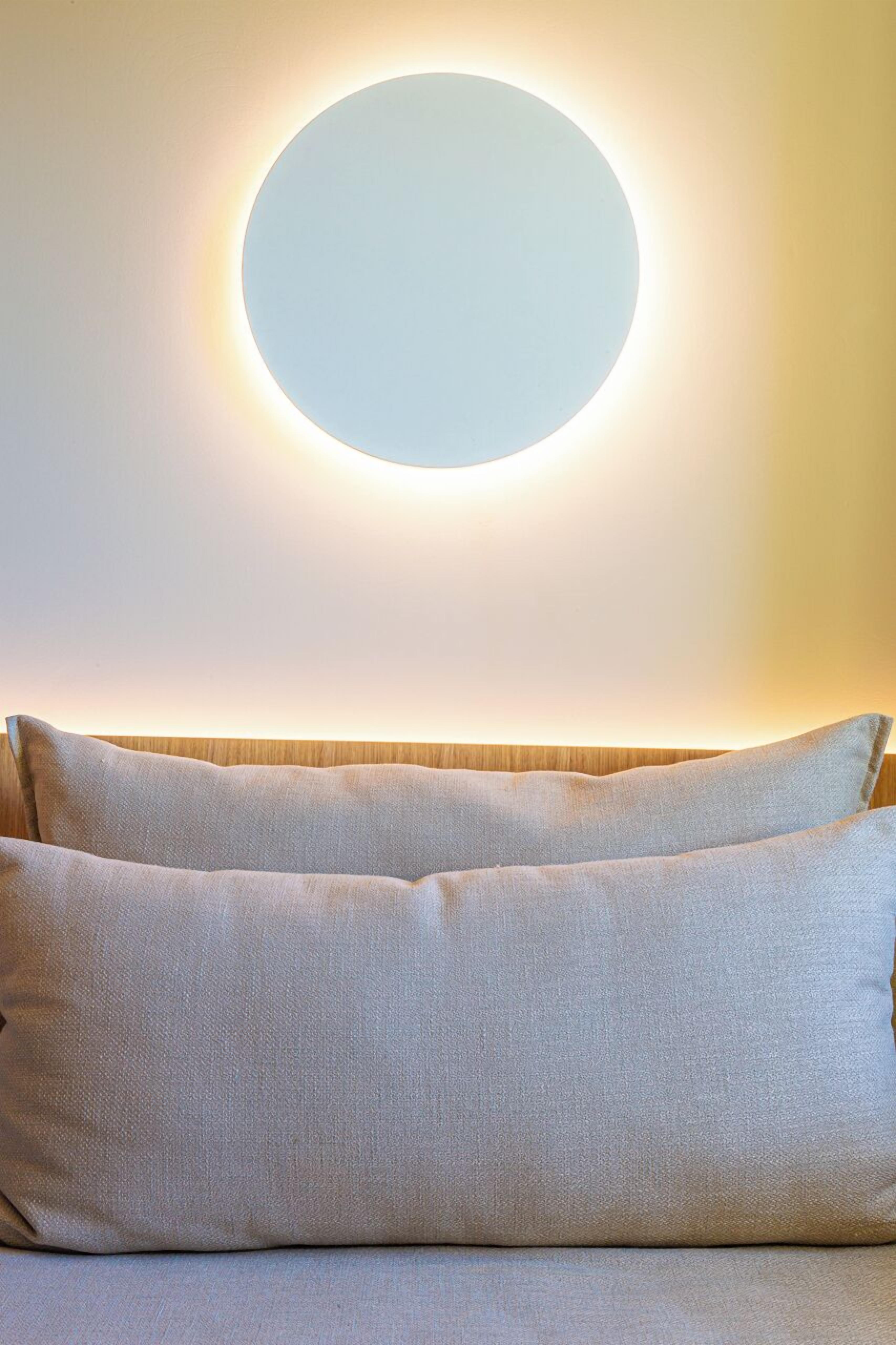 Una habitación con una lámpara circular sobre la cama, con dos almohadas.