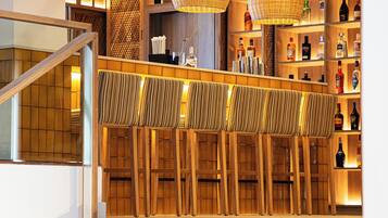 A bar area with wicker pendant lighting, wooden bar stools, and shelves stocked with liquor bottles.