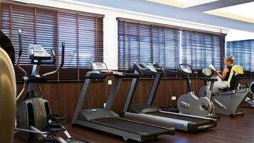 Una palestra con diverse tapis roulant ed ellittiche, pavimenti in legno e ampie finestre dotate di persiane.