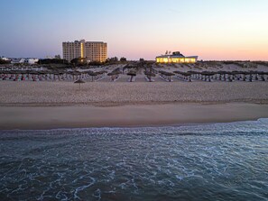 A beach with rows of umbrellas and lounge chairs, a building with a balcony overlooking the beach, and a hotel with a pool area. - Ozadi Altura Beach Resort  (Castro Marim)