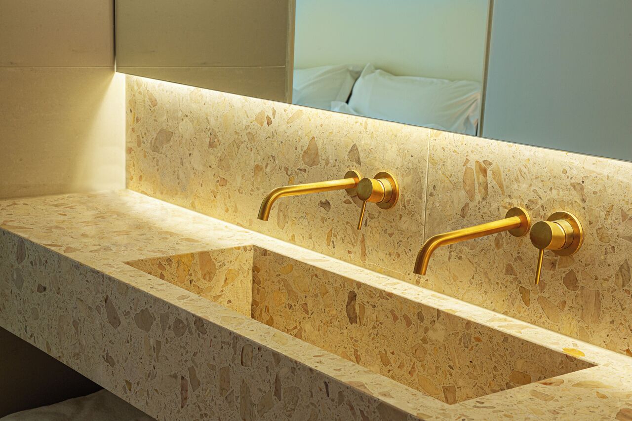 Un baño con encimera de mármol y detalles dorados.