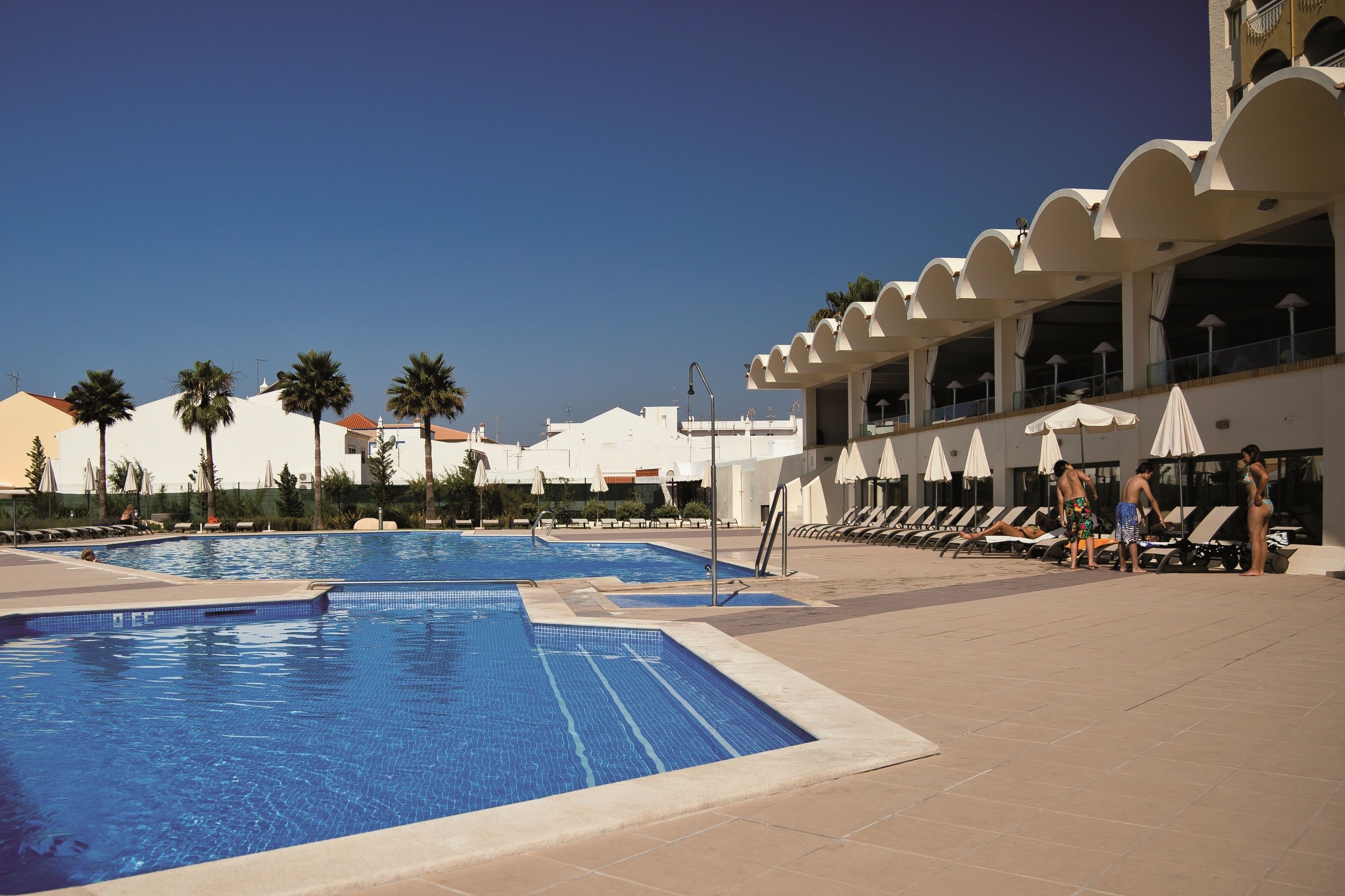 Un espace piscine comprenant plusieurs bassins, des chaises longues et des parasols.