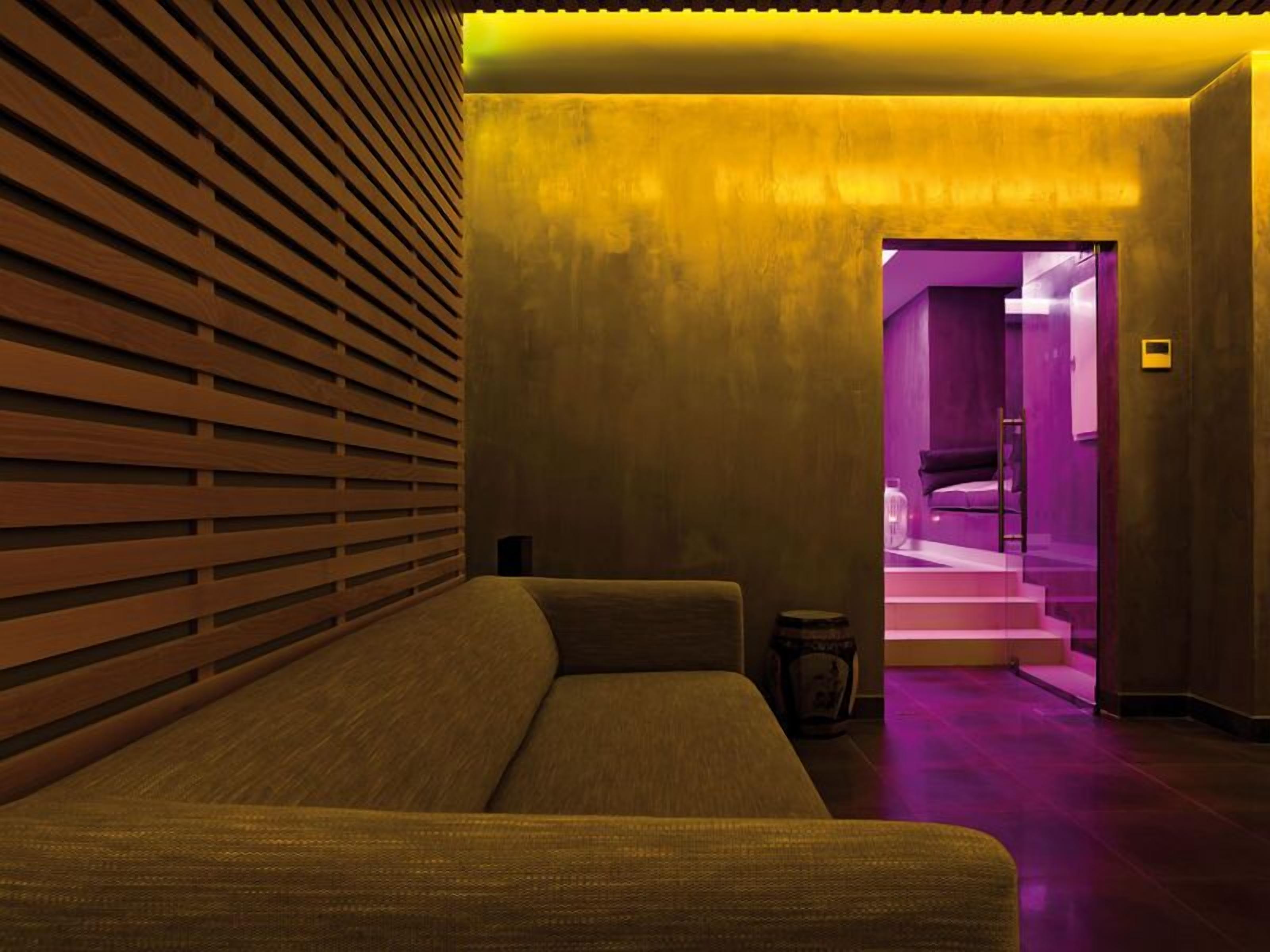 Un interior moderno con un sofá, una mesita y una escalera que conduce a una habitación iluminada en tonos morados.
