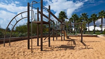 Explore the playground's climbing frame and slide amidst lush palm trees.