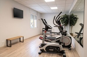 Un gimnasio con equipo de ejercicio, una banca y un televisor en la pared.