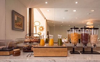 Un bufé de desayuno con diversas opciones de alimentos y bebidas, entre ellos cereales, frutas y jugos.
