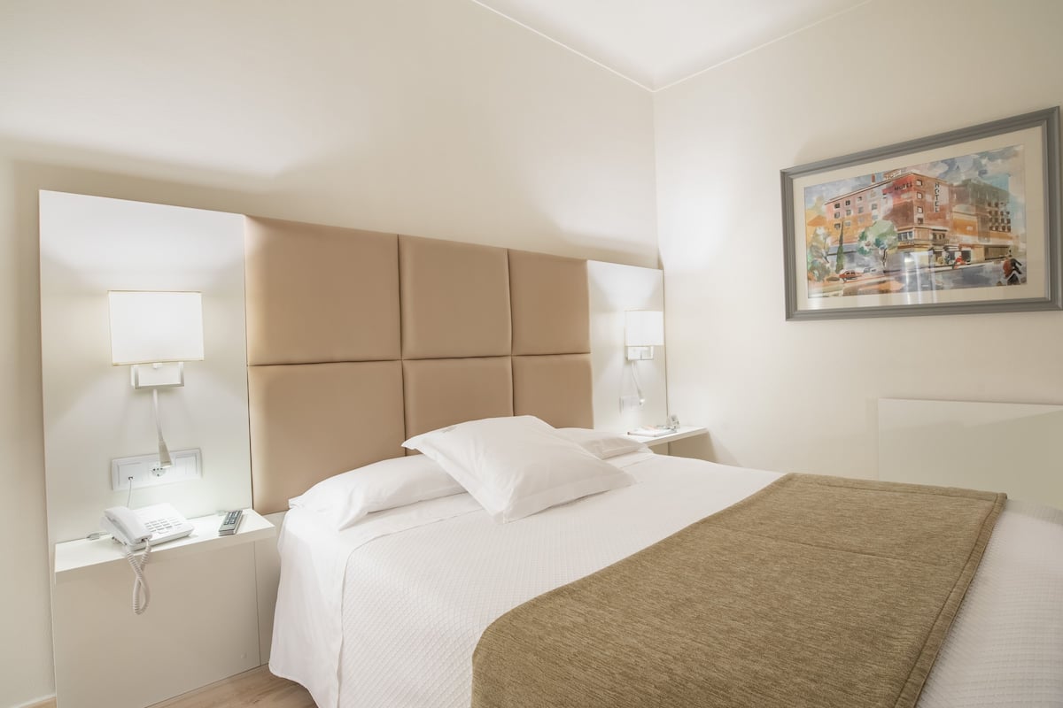A hotel room with a large bed, a headboard, bedside lamps, a phone, and a painting on the wall.