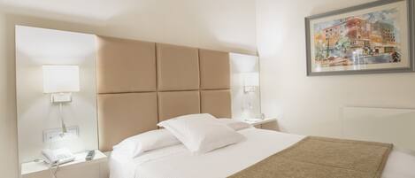 Habitación de hotel con una cama grande, cabecera, lámparas de noche, teléfono y un cuadro en la pared.