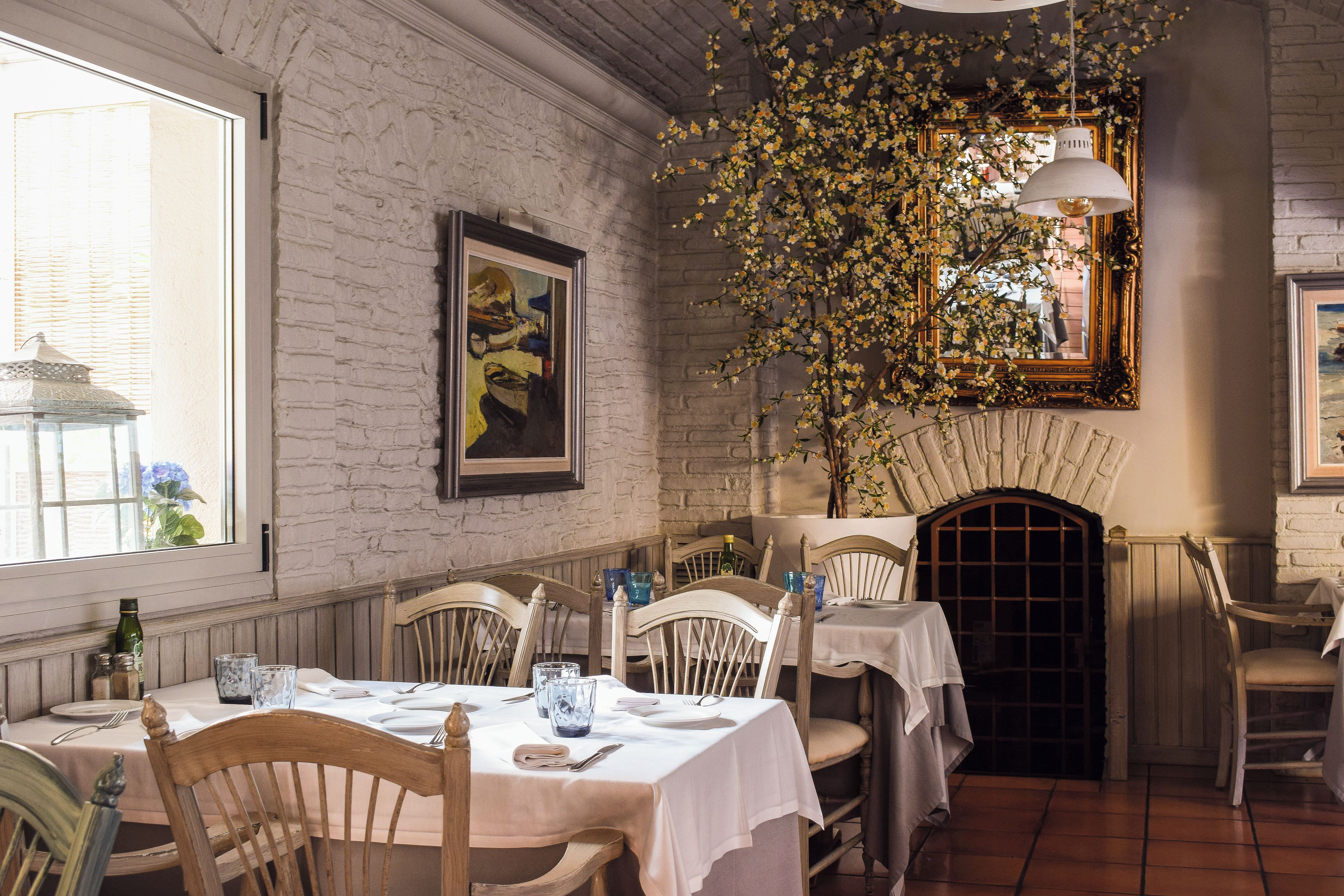 Un comedor con paredes de ladrillo blanco, sillas de madera y mesas dispuestas para una comida.