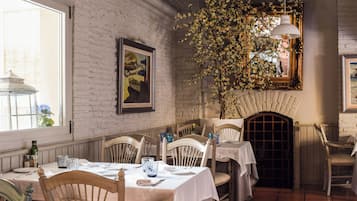 Un comedor con paredes de ladrillo blanco, sillas de madera y mesas dispuestas para una comida.