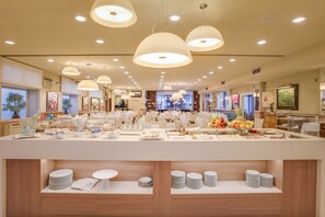 A well-lit buffet area with multiple serving stations, a variety of food items, and neatly arranged tableware. - Hotel Pirineo Figueres by Pierre and Vacances (Figueres)