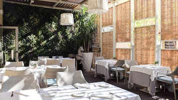 An outdoor dining area with tables set for two, surrounded by wicker furniture and a decorative horse statue.