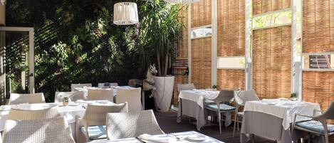 An outdoor dining area with tables set for two, surrounded by wicker furniture and a decorative horse statue.