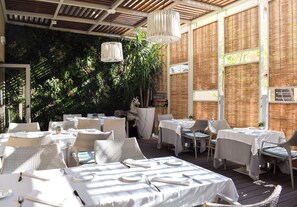 An outdoor dining area with tables set for two, surrounded by wicker furniture and a decorative horse statue. - Hotel Pirineo Figueres by Pierre and Vacances (Figueres)