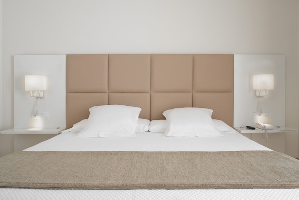 Una cama bien hecha con un cabecero color beige, ropa de cama blanca y dos lámparas de noche.