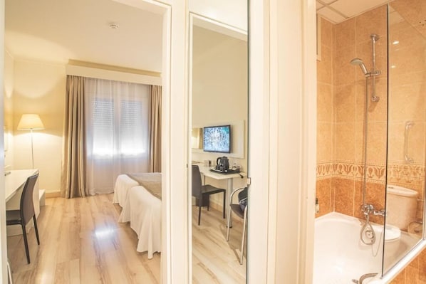Habitación de hotel con cama, escritorio, televisión y zona de ducha.