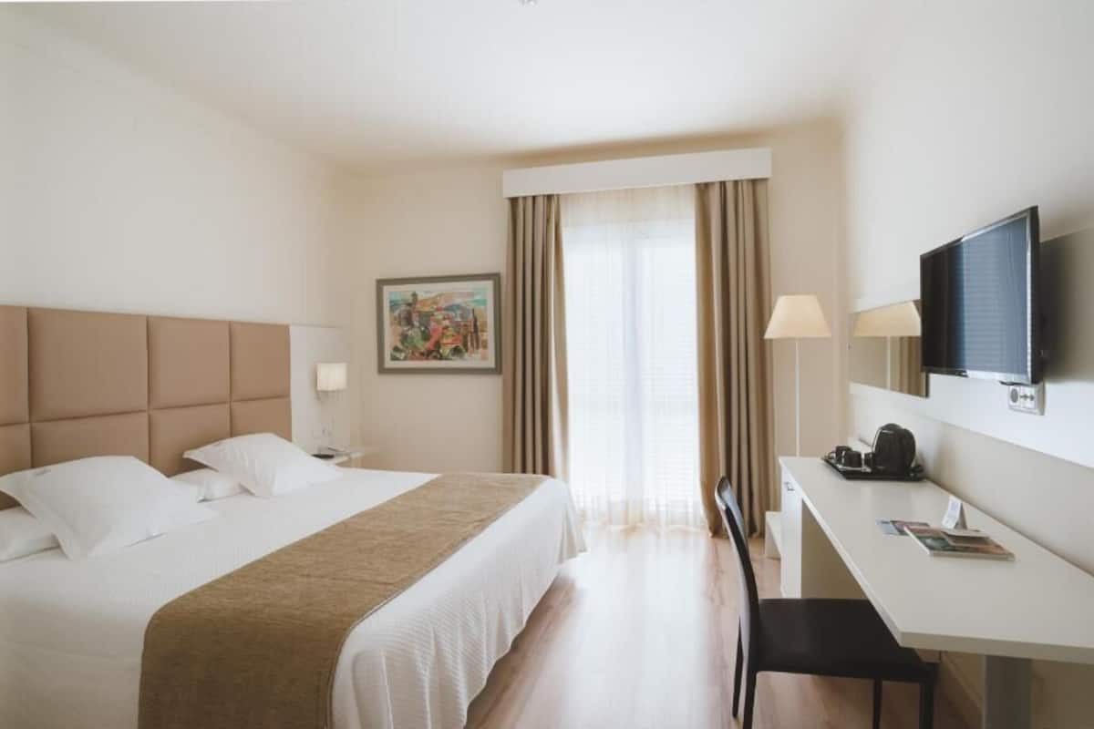 A hotel room with a bed, desk, chair, TV, and curtains.
