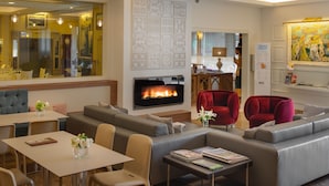 A modern hotel lobby with a fireplace, seating areas, and a dining space. - Hotel Pirineo Figueres by Pierre and Vacances (Figueres)