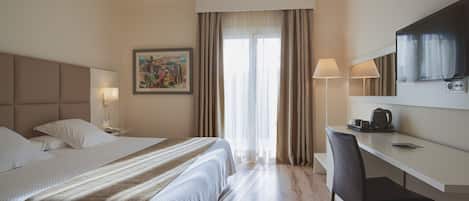 Une chambre d’hôtel avec un lit, un bureau, une chaise, une lampe, un tableau et une fenêtre avec des rideaux.