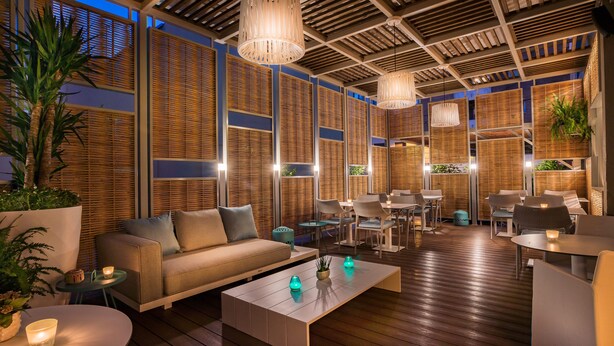 A modern outdoor lounge area with wooden flooring, a sofa, tables, and chairs. - Hotel Pirineo Figueres by Pierre and Vacances (Figueres)