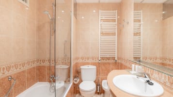 Une salle de bain moderne dotée d’une douche à parois de verre, d’une baignoire, de deux toilettes et d’un lavabo avec un plan de travail en verre.