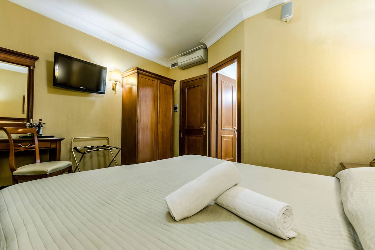 A hotel room with a bed, a TV mounted on the wall, a desk with a chair, and a door.