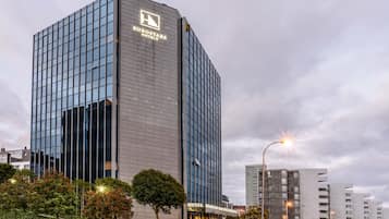 Un hotel moderno con fachada de vidrio, un logotipo destacado y una entrada bien iluminada.