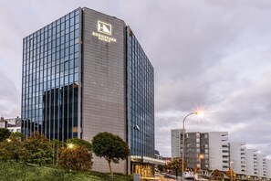 Ein modernes Hotel mit Glasfassade, einem gut sichtbaren Logo und einem hell erleuchteten Eingang.