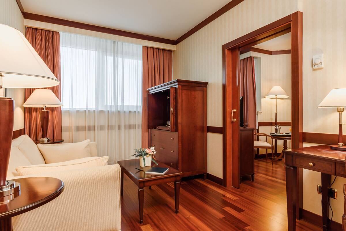 Une chambre d’hôtel avec un plancher en bois, un canapé, une table avec une lampe, une armoire et un miroir.
