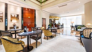 A spacious lobby with high ceilings, a central seating area with tables and chairs, and a large window providing natural light. - Eurostars Gran Hotel Santiago (Santiago de Compostela)