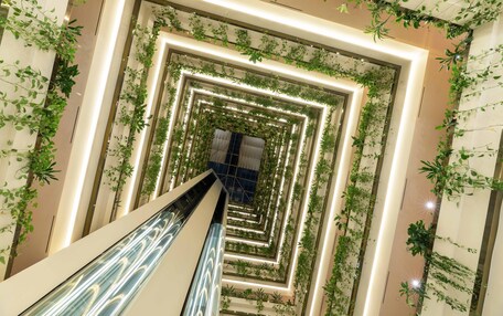 A modern interior with a central spiral staircase surrounded by greenery and illuminated by recessed lighting.
