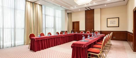 Un salón de conferencias con una larga mesa, sillas rojas y un candelabro.