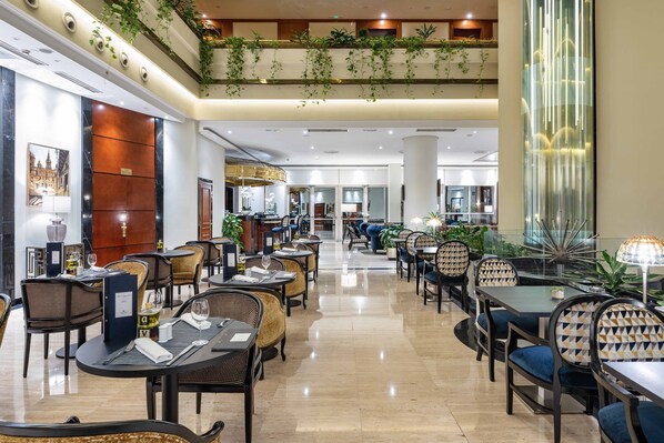 Un amplio hall de hotel con varias zonas de comedor, una recepción y vistas al piso superior.
