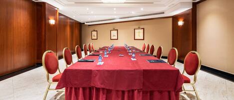 Une salle de conférence avec une longue table, une nappe rouge et des chaises assorties.