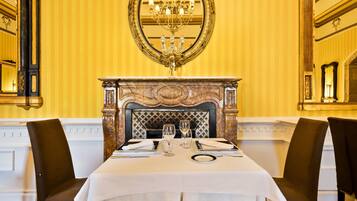 Un comedor formal con una mesa dispuesta para dos personas, chimenea y decoraciones ornamentales en las paredes.