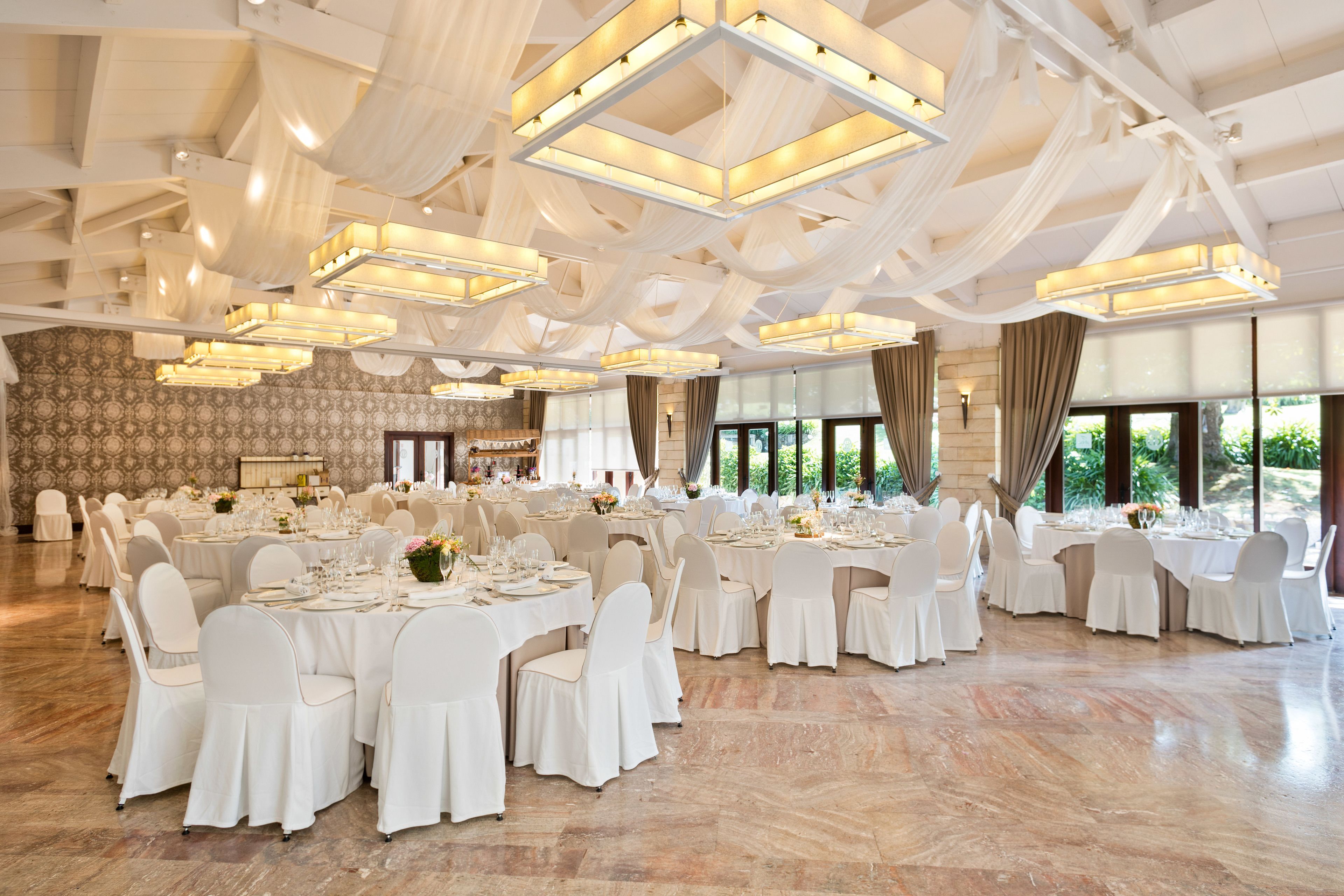 Un salón de banquetes con mesas redondas, sillas blancas y candelabros.