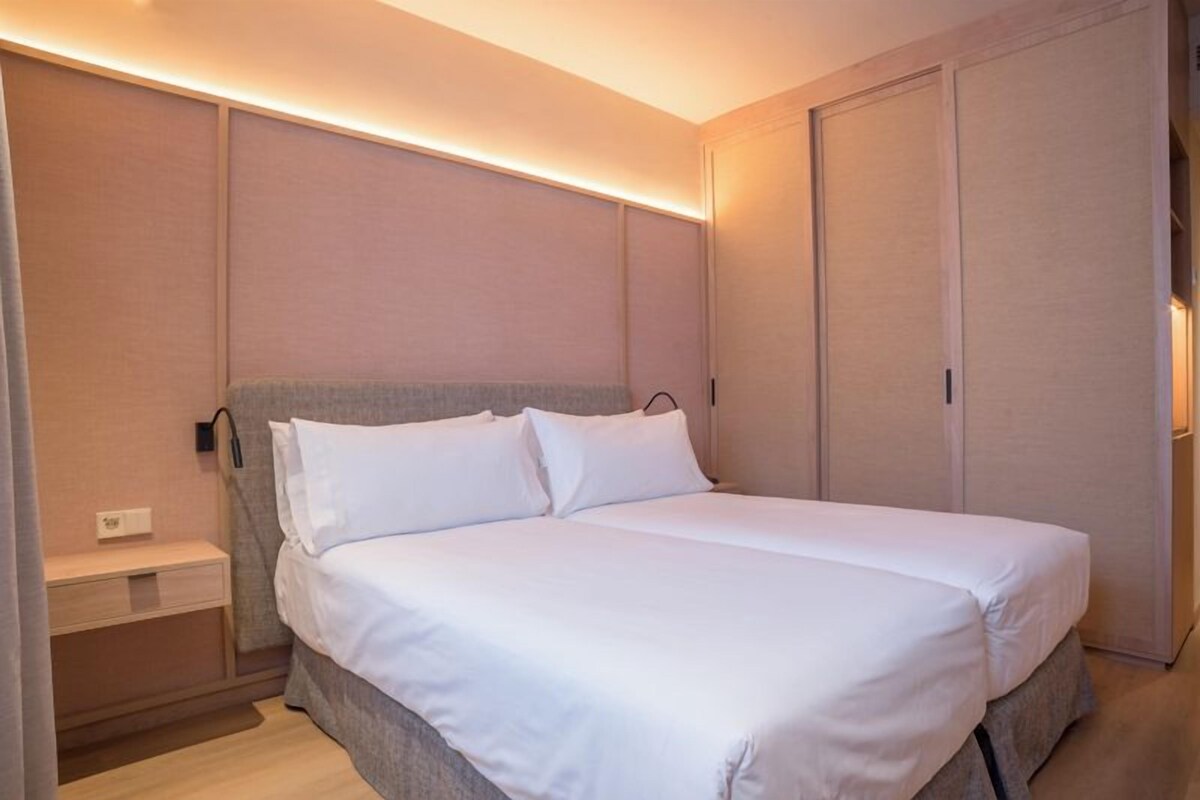 Una cama individual bien hecha con sábanas blancas, una mesita de noche y una lámpara de pared.