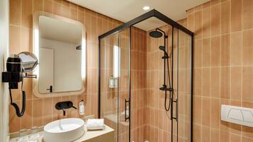 Een moderne badkamer met een douchecabine van glas, een rond wastafel, een spiegel en een haardroger.